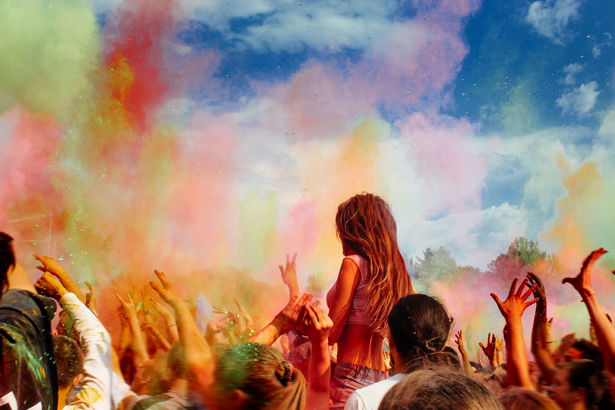 happy people crowd partying under colorful powder cloud at holi